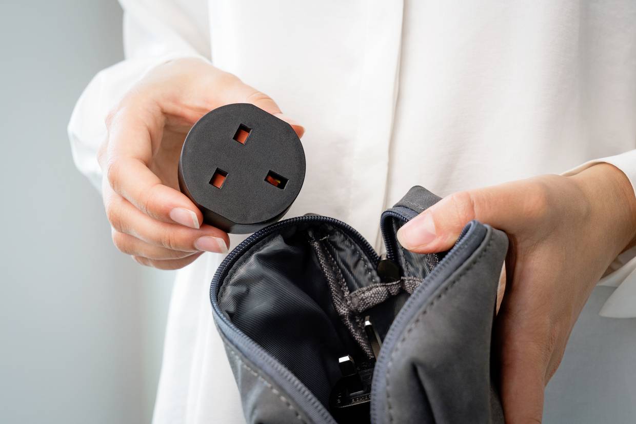 Eine Person hält einen Adapterstecker und verpackt ihn in eine graue Tasche. Der Fokus liegt auf den Händen und dem Stecker.