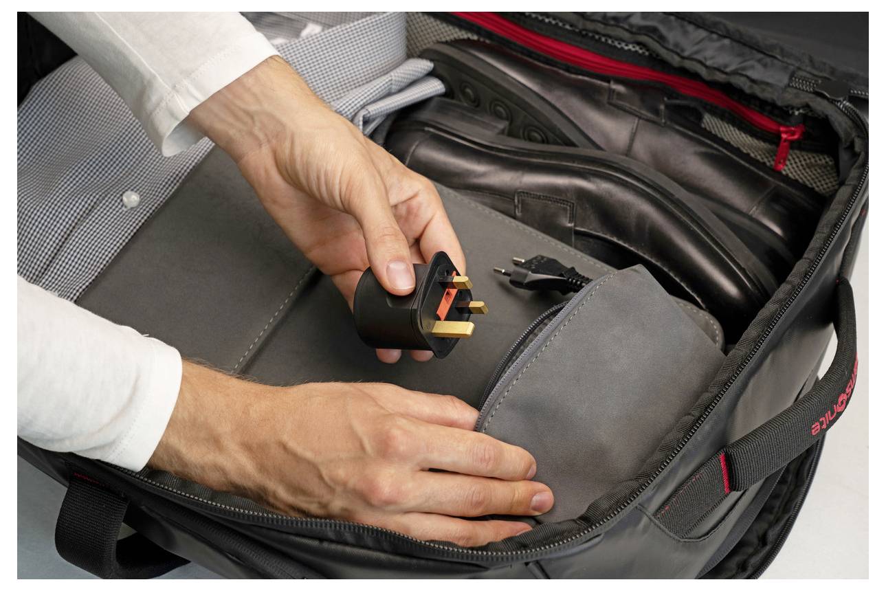 Hände, die einen dreipoligen Stromstecker halten, während sie ihn in eine schwarze Reisetasche stecken, was die Verborgenheit eines Geräts suggeriert.