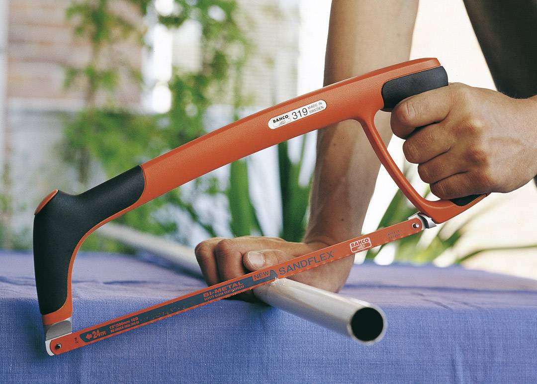 Eine Person verwendet eine Bügelsäge, um ein Metallrohr zu schneiden. Die rote Säge hat einen schwarzen Griff.