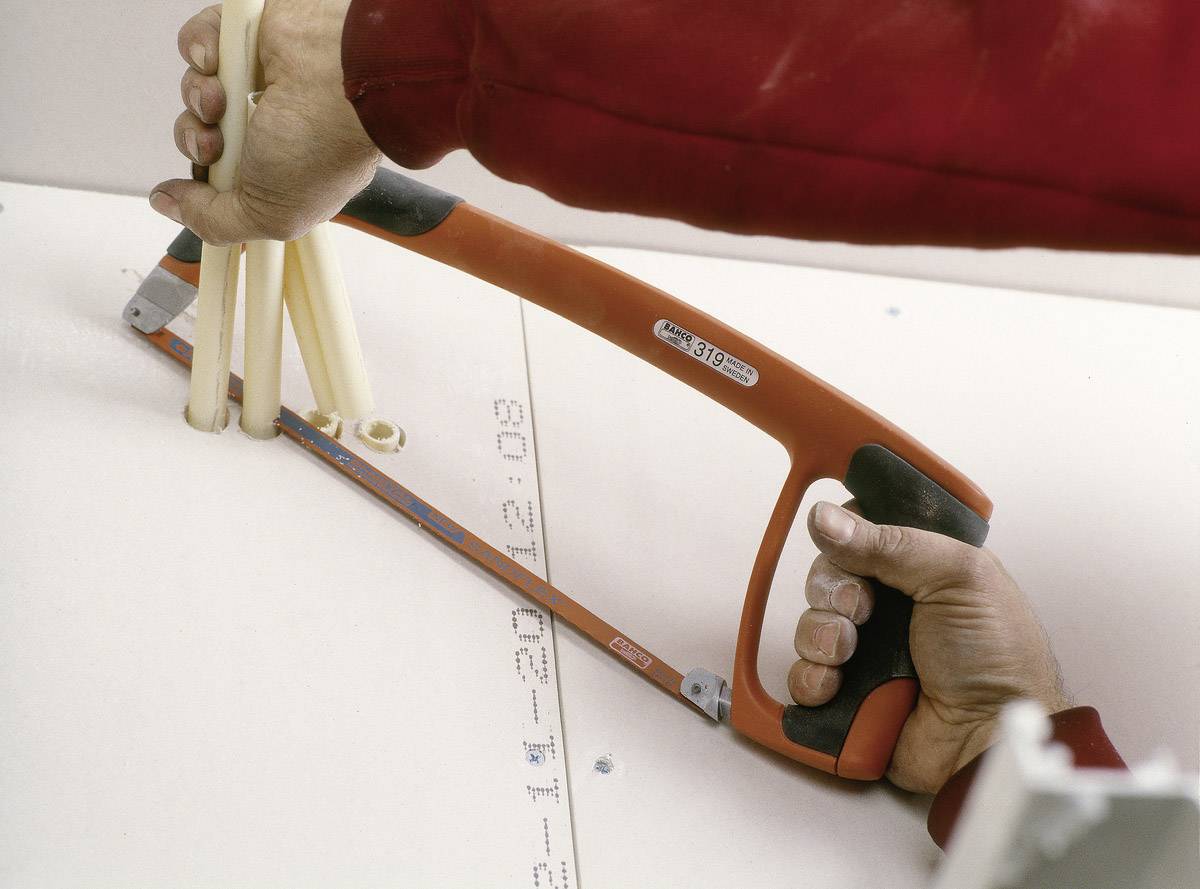 Person schneidet weiße Kunststoffrohre mit einer Handsäge. Rohre sind in einer Halterung fixiert, um präzise Schnitte zu ermöglichen.