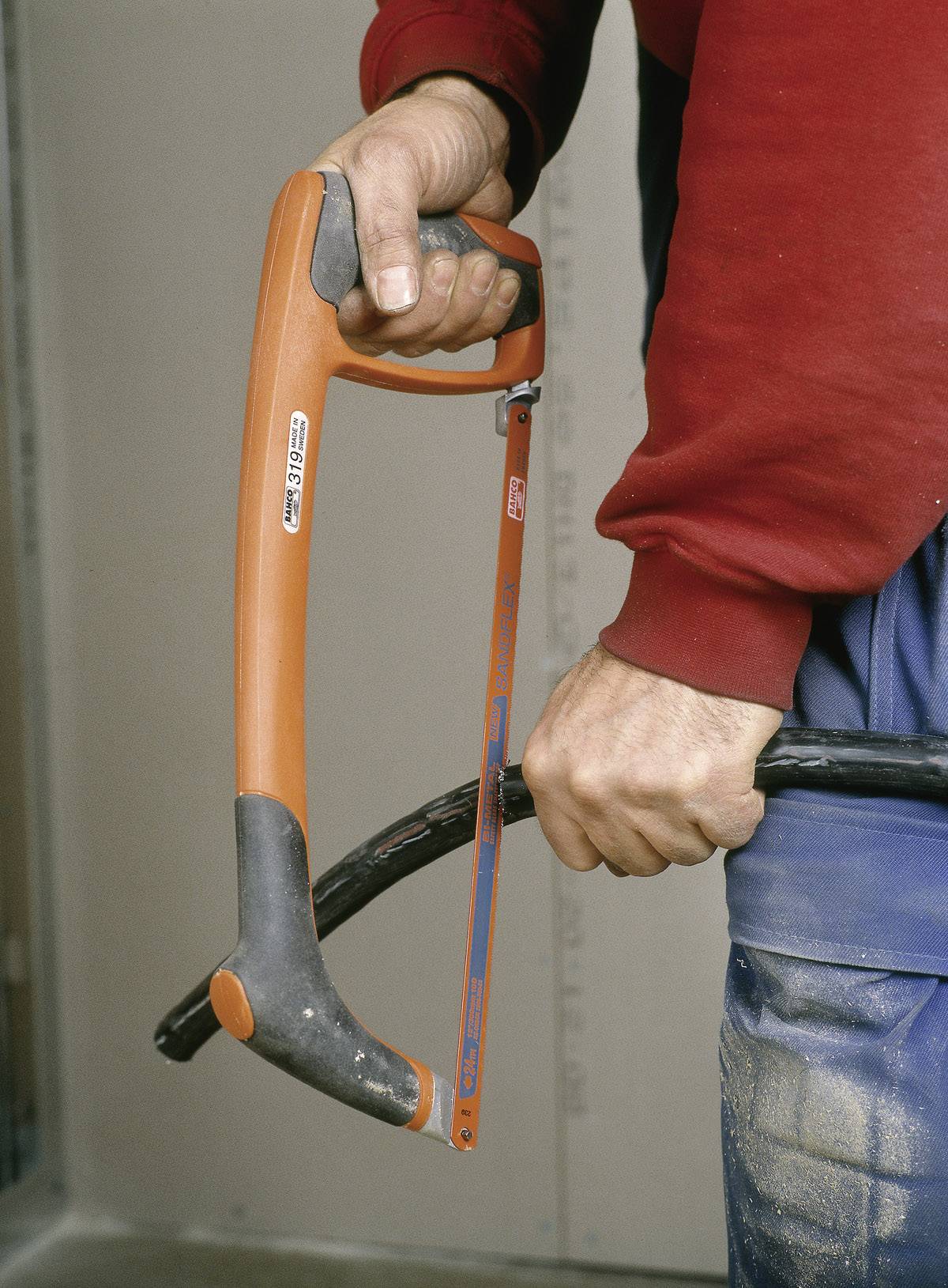 Eine Person in Arbeitskleidung hält eine Bügelsäge und ist dabei, ein dickes schwarzes Kabel zu durchtrennen.