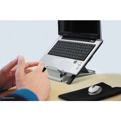 Ein Laptop steht auf einem verstellbaren Ständer auf einem Schreibtisch. Daneben liegen eine Computermaus und ein Mauspad. Hände tippen auf der Tastatur.