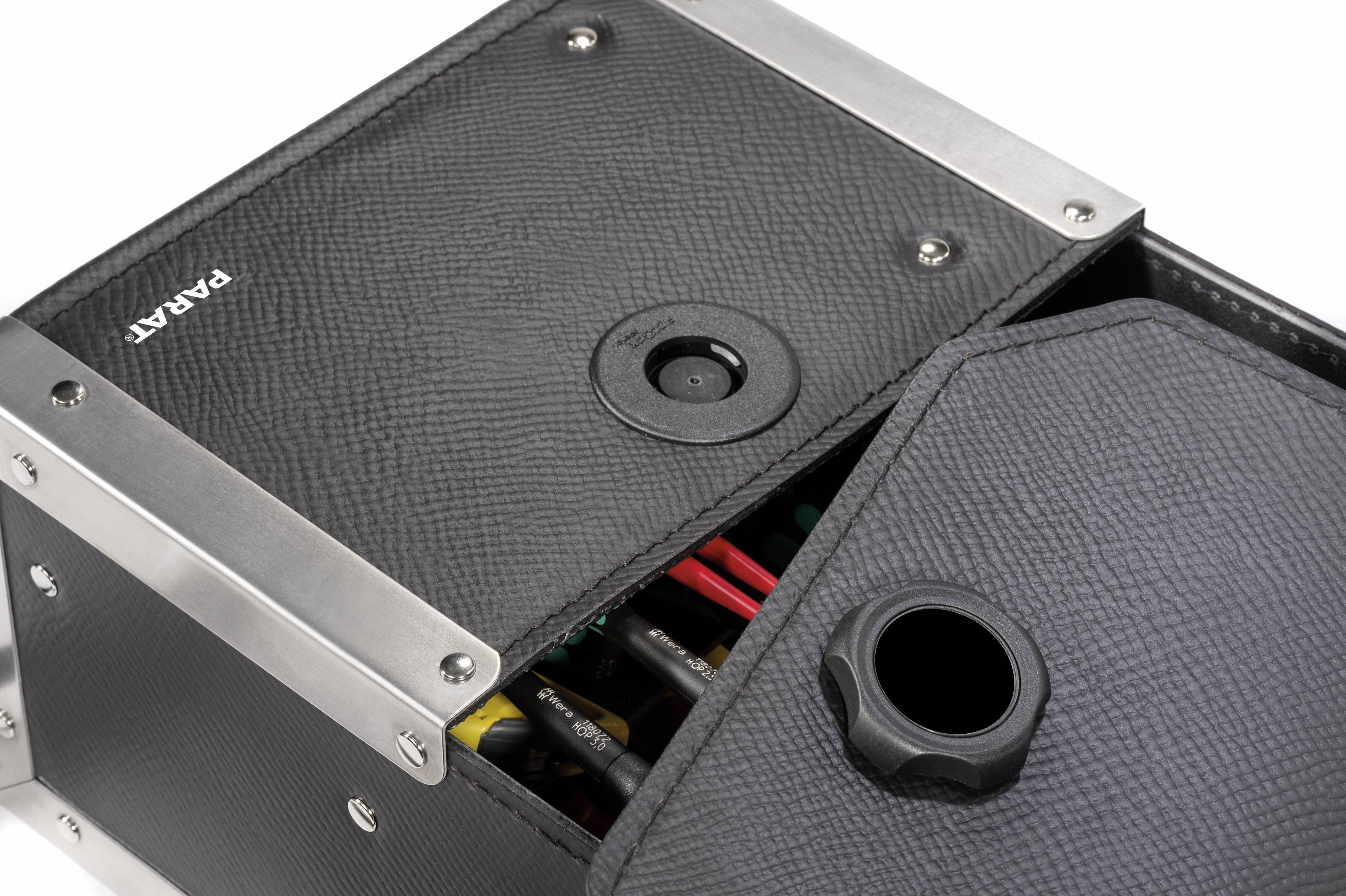 Das Bild zeigt eine elegante, schwarze Box mit Metallkanten und einer geöffneten Klappe. Im Inneren sind verschiedene Werkzeuge sichtbar.