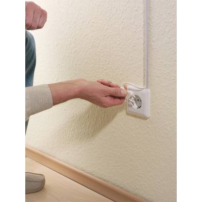 Eine Person steckt das Stromkabel eines Geräts in eine Steckdose an einer Wand ein.