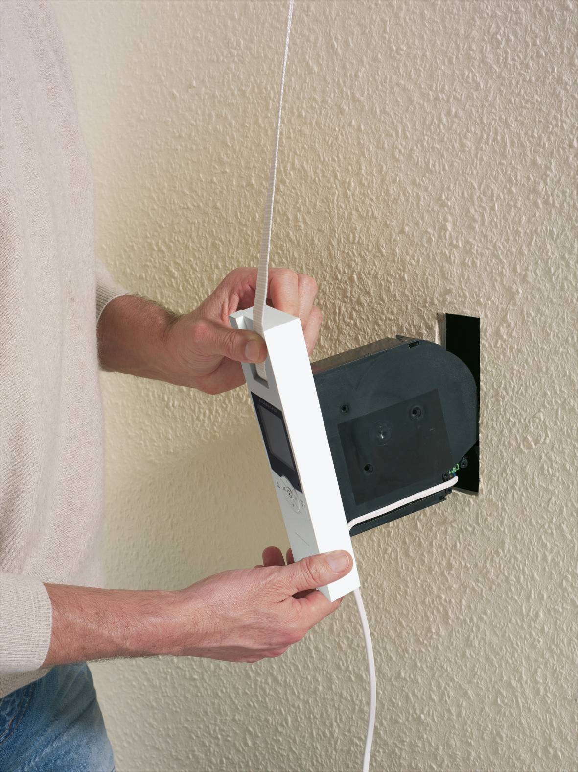 Eine Person installiert ein weißes Thermostat an der Wand, indem sie es an einen bereits eingebauten schwarzen Kasten anschließt.