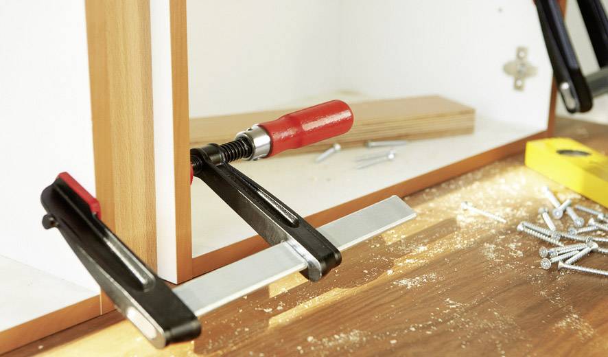 Ein Holzschrank im Bauprozess mit Klemmen, Schrauben und Holzspänen auf einer Werkbank.