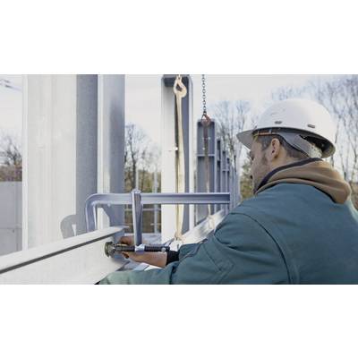 Ein Bauarbeiter montiert Stahlträger auf einer Baustelle. Er trägt einen Schutzhelm und eine grüne Jacke. Es ist ein klarer Tag.