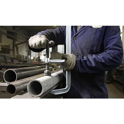 Eine Person in Arbeitskleidung klemmt Metallrohre mit einer großen Schraubzwinge in einer Werkstatt.