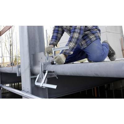 Eine Person kniet auf einem Stahlträger und befestigt Metallklemmen. Sie trägt Arbeitskleidung und Handschuhe, was auf eine Baustelle hinweist.