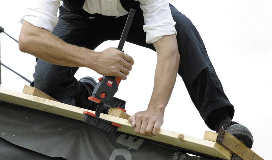 Eine Person arbeitet auf einem Dach und verwendet eine Zwinge, um Holz zu befestigen.