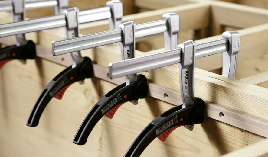 Mehrere Metallzwingen klemmen Holzbretter zusammen.