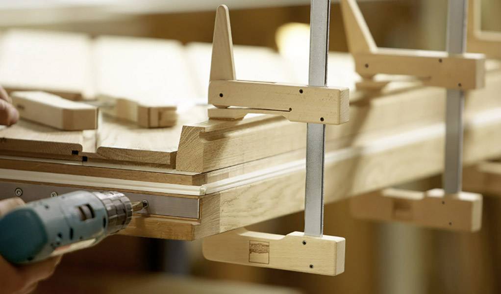Holzbearbeitung: Eine Person nutzt eine Bohrmaschine zum Zusammenfügen von Holzplatten, die mit Klemmen fixiert sind.