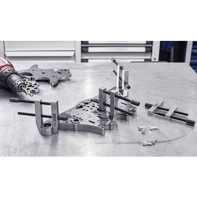 Werkbank mit Metallteilen, Schrauben, Klemmen und Bohrer. Teile scheinen vorbereitet für Maschinenbau oder Montage.