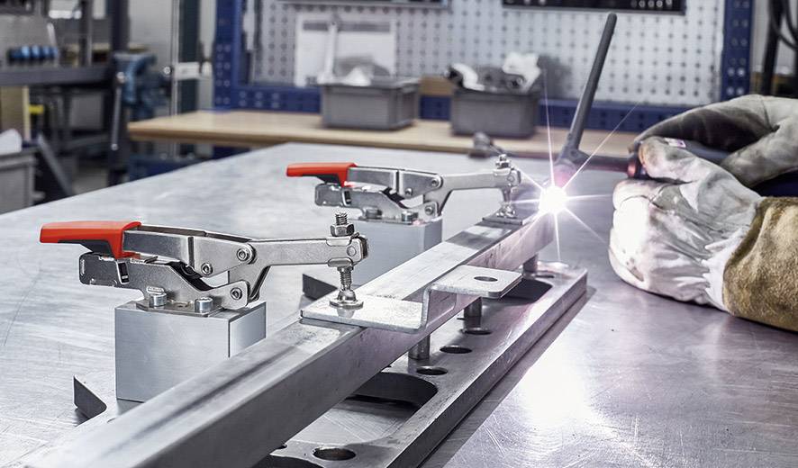 Eine Person führt in einer Werkstatt präzises Schweißen an einem Metallwerkstück durch. Klemmen halten das Werkstück stabil.