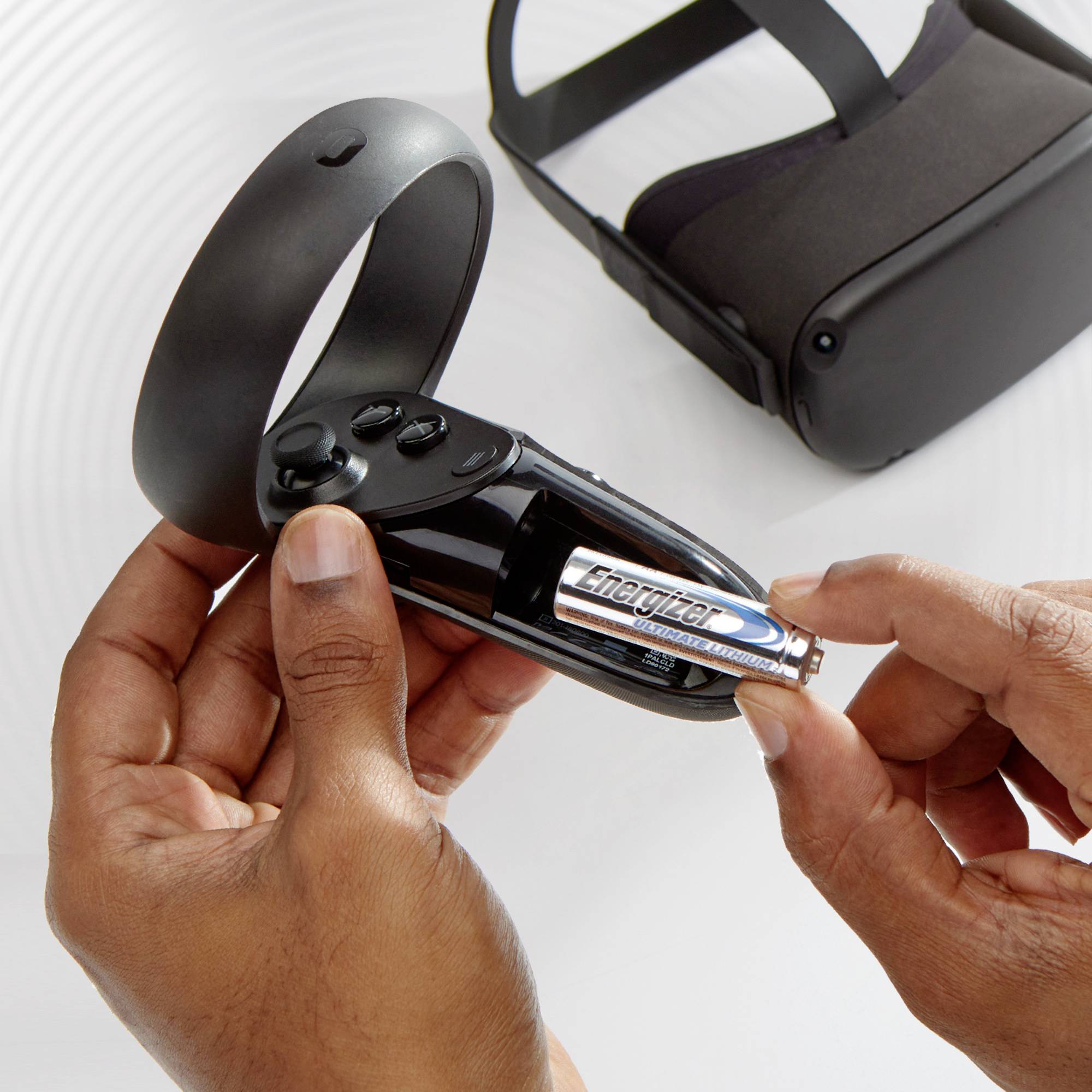 Eine Person wechselt die Batterien in einem kabellosen VR-Controller; ein VR-Headset liegt daneben auf einem Tisch.