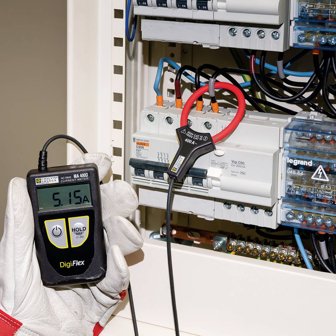 Ein Elektriker misst den Stromfluss in einem Sicherungskasten mit einem digitalen Messgerät, das '5.15 A' anzeigt.