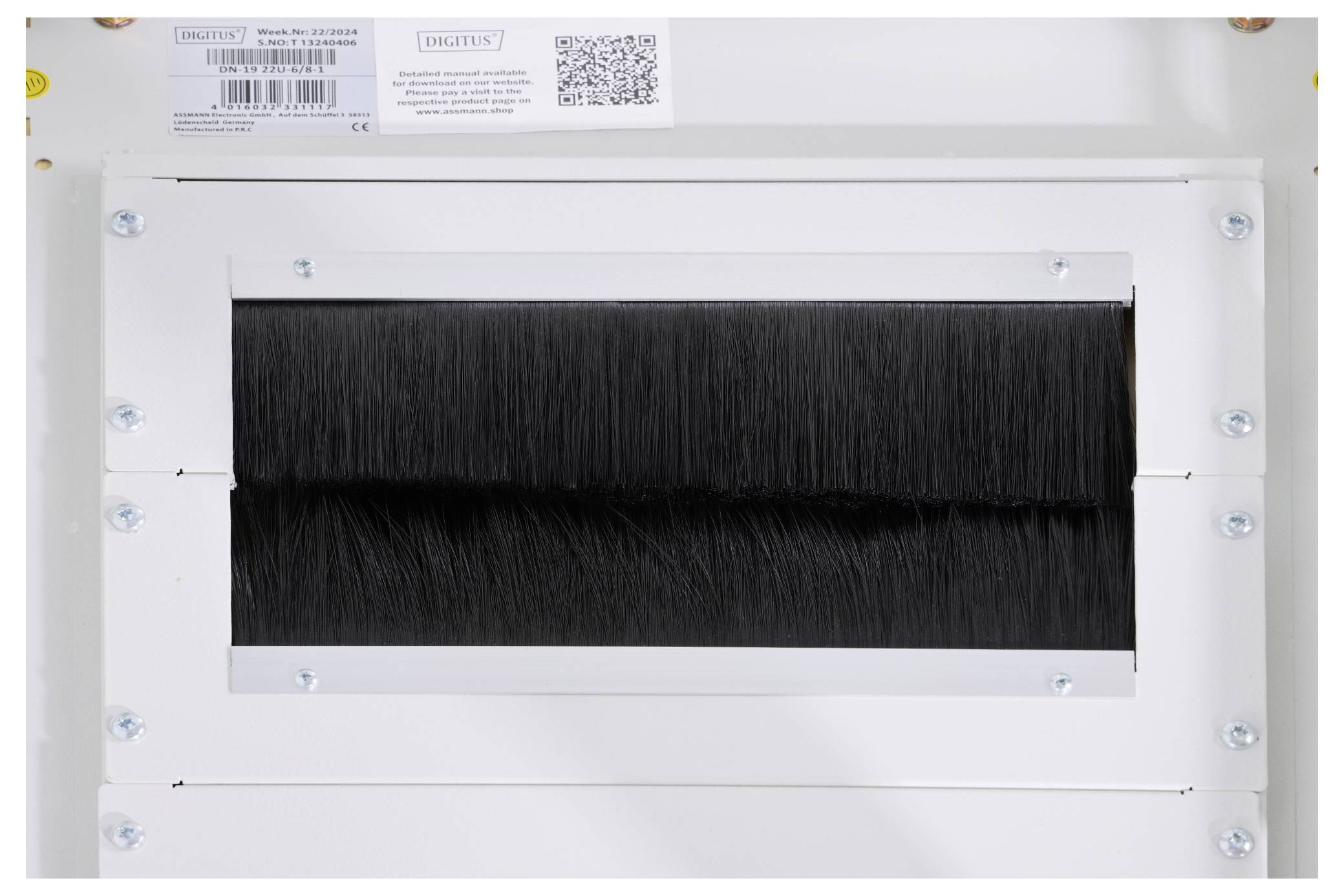 Ein rechteckiger Lufteinlass mit schwarzer Bürstendichtung. Oben ein Etikett mit Produktinformation und QR-Code.