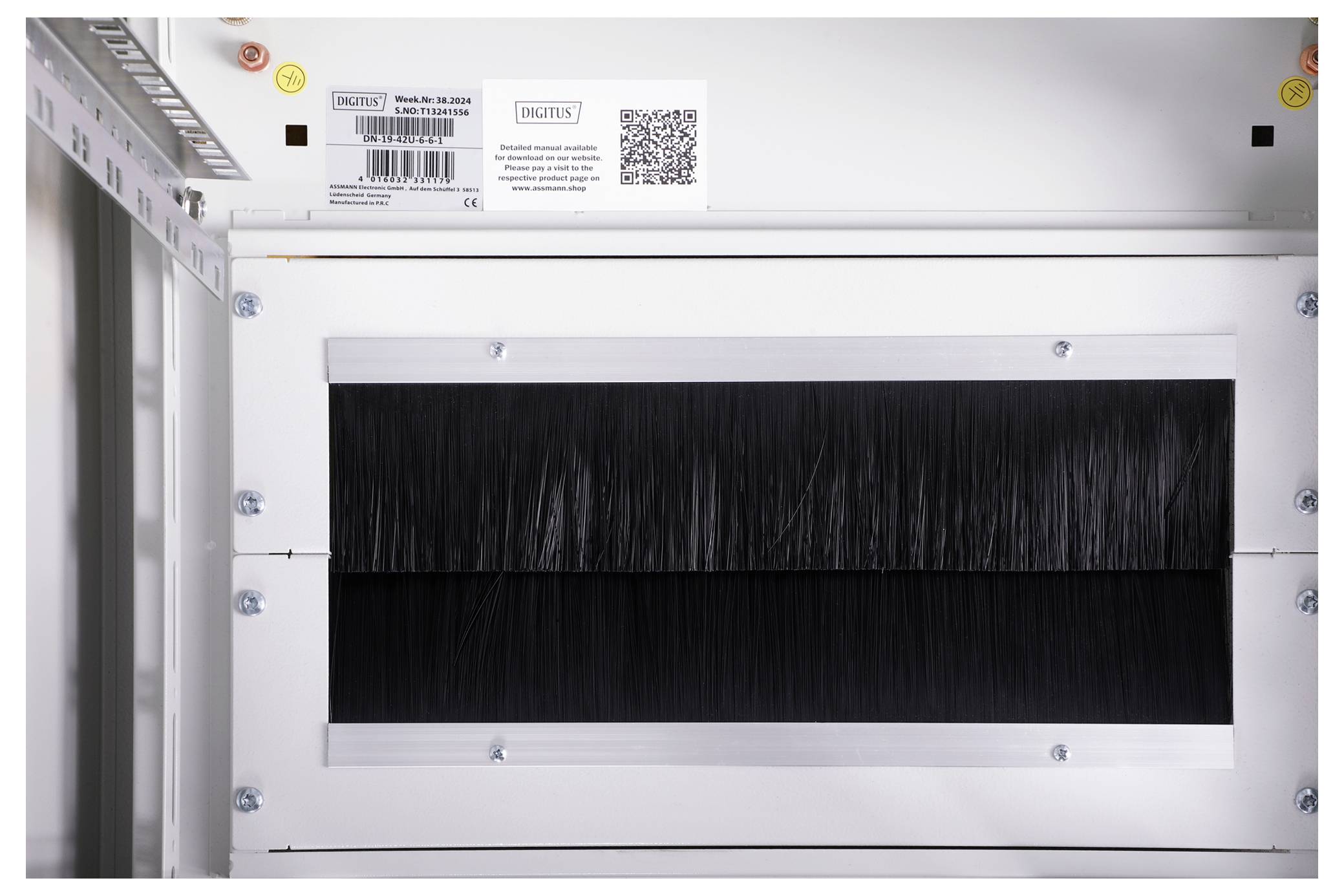 Ein weißer Kasten mit schwarzer Bürstenleiste in der Mitte; oben ein Barcode und ein QR-Code mit Text über eine Montagedose.