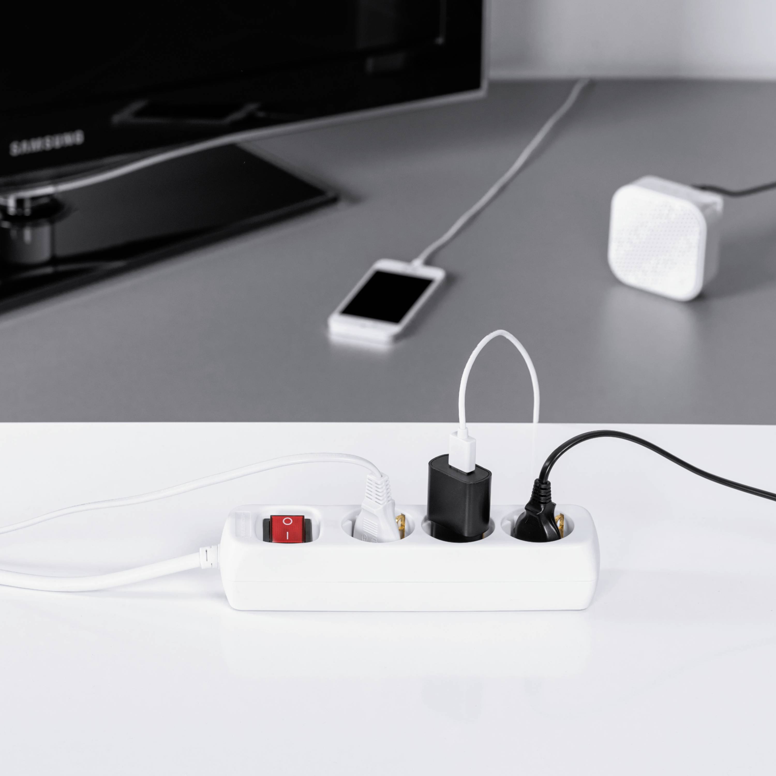 Mehrfachsteckdose mit mehreren Geräten eingesteckt: TV, Smartphone und Lautsprecher, zeigt Elektronik im Wohnzimmer.