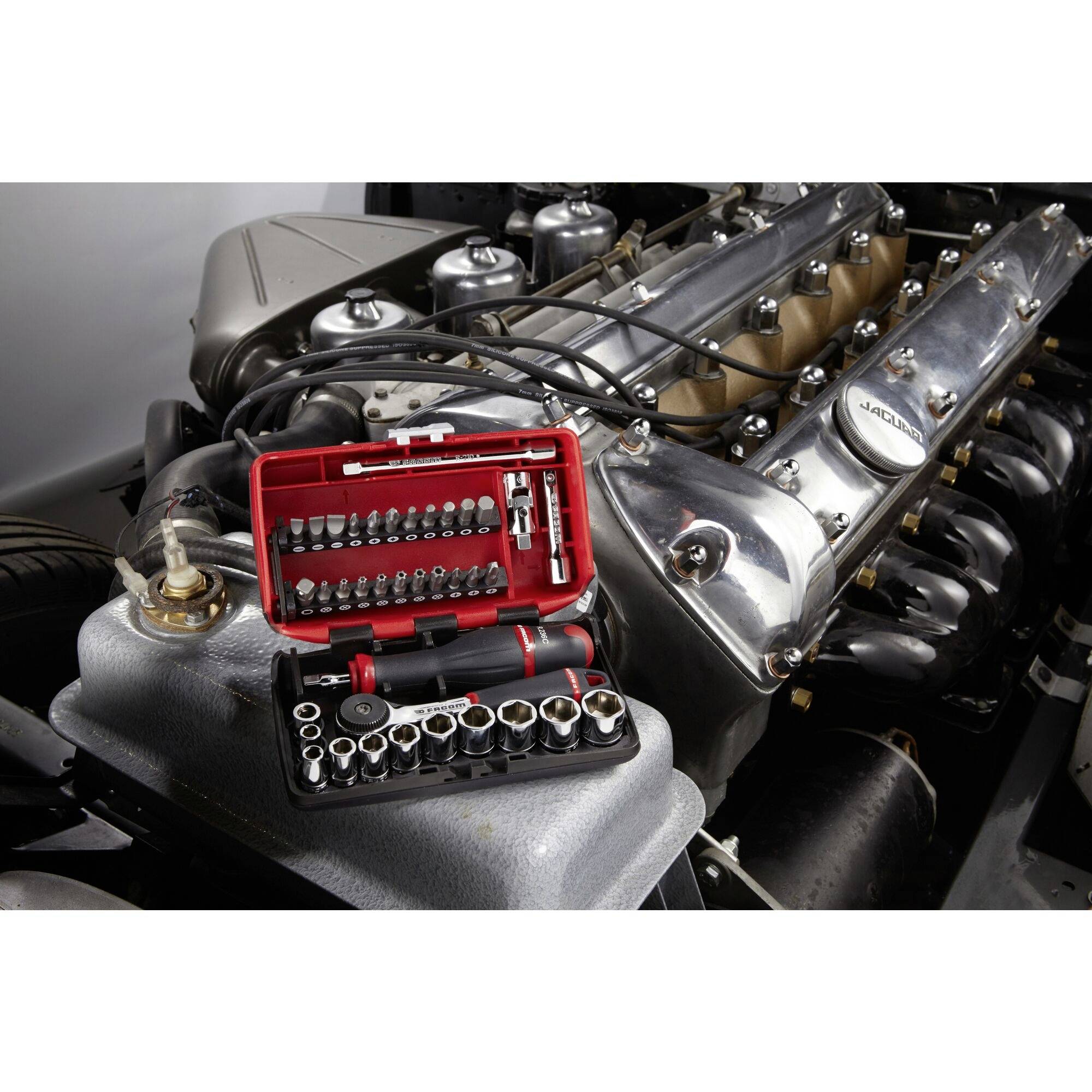 Werkzeugkoffer mit Steckschlüsseln liegt auf einem alten, silbernen Automotor. Motor hat sichtbare Zündkabel und Bauteile.