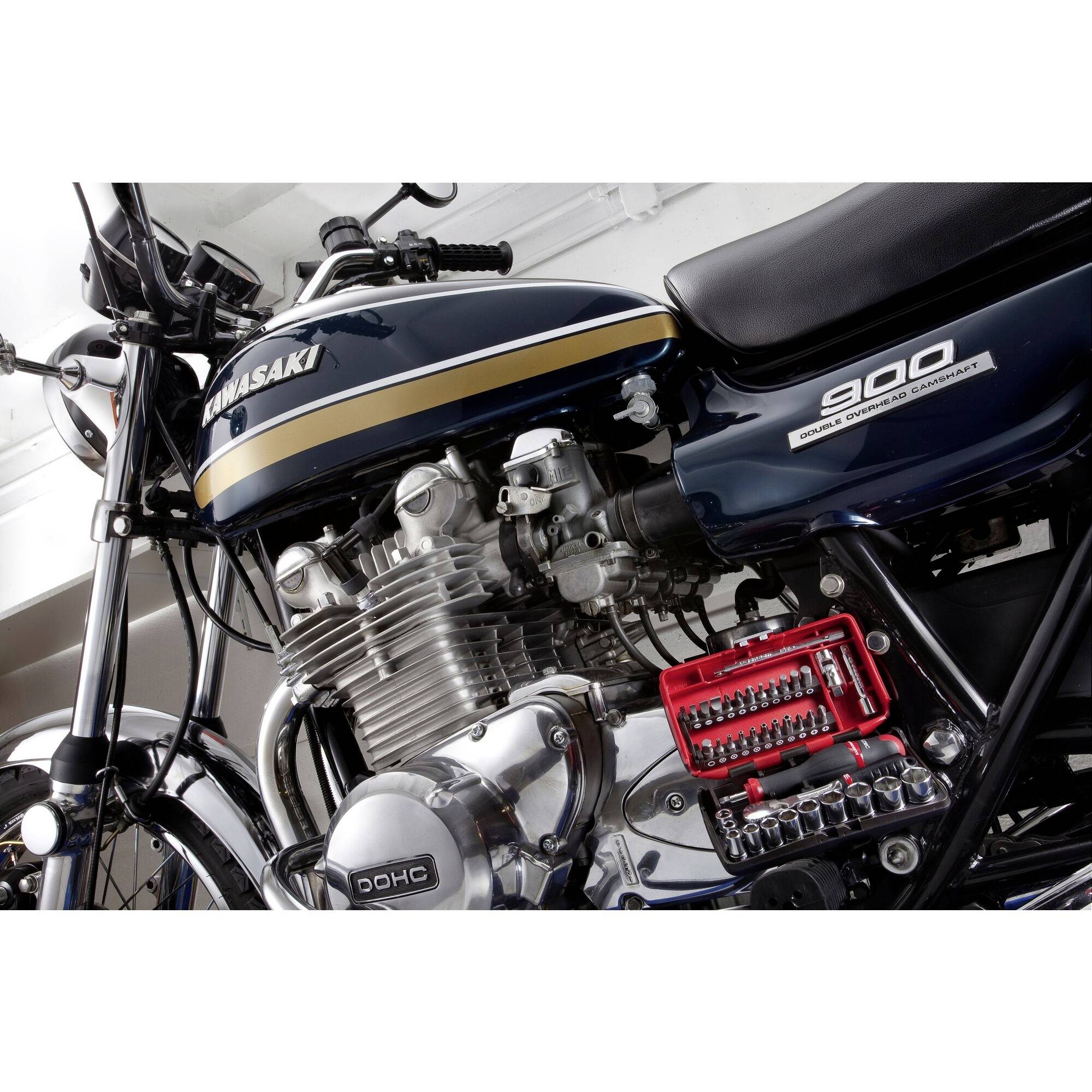 Ein Motorrad mit dem Schriftzug 'Kawasaki' und '900' auf der Verkleidung, silbernen Motorenteilen und einem roten Werkzeugkasten.