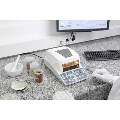 Ein Laborarbeitsplatz mit einem Feuchtemessgerät, umgeben von Probenbehältern und einem Computerbildschirm, auf dem Daten angezeigt werden.