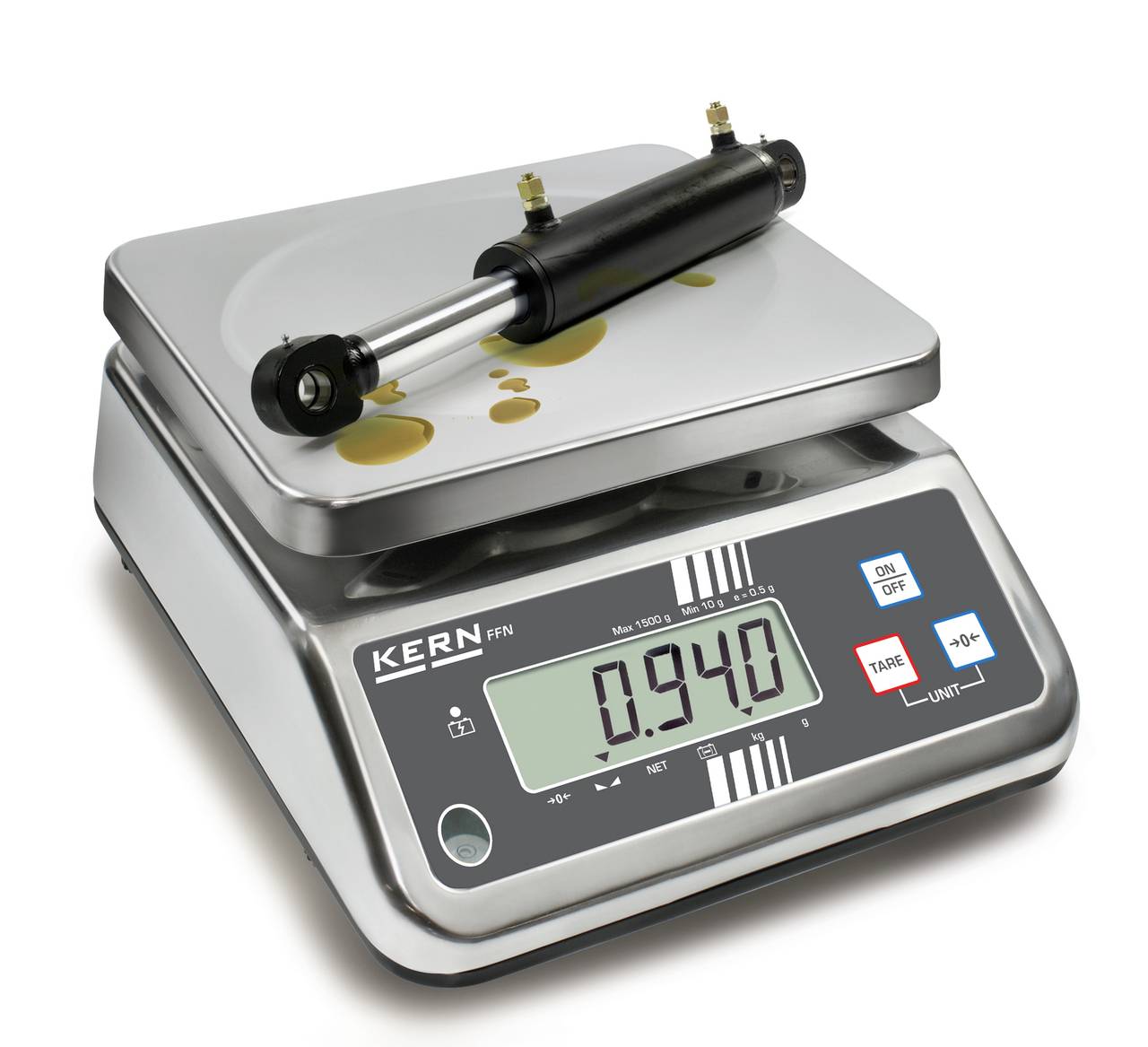 Eine digitale Waage zeigt das Gewicht eines zylinderförmigen Metallteils auf dem Display '0,940'.