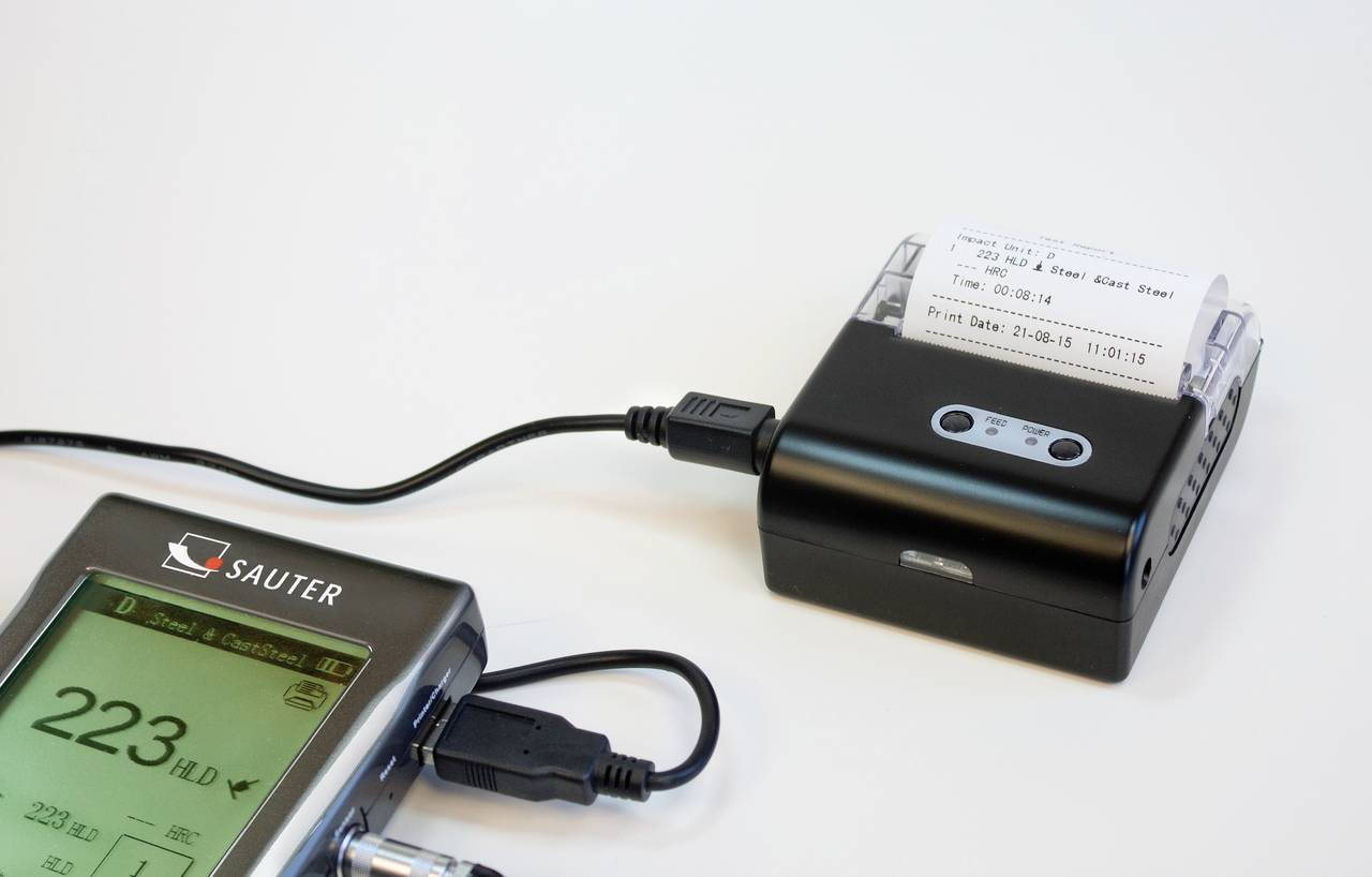 Ein Gerät zur Überwachung von Feinstaub, verbunden mit einem Stromkabel. Ein kleiner Bildschirm zeigt das Datum '21-08-15'.