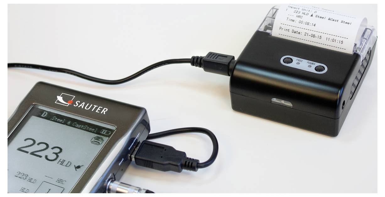 Ein elektronisches Messgerät und ein Drucker sind durch ein Kabel verbunden. Der Drucker gibt einen Beleg mit Messdaten aus.