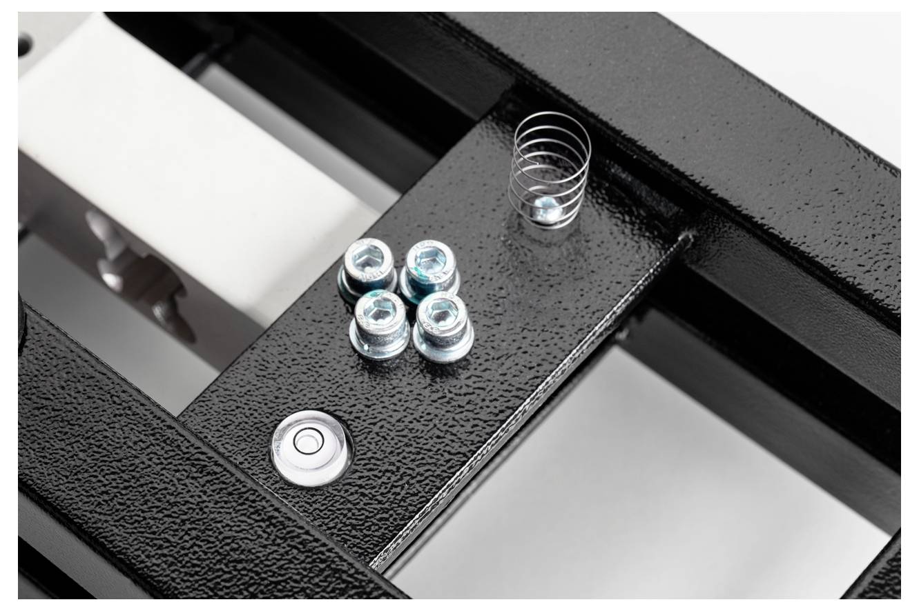 Eine schwarze Metallstruktur mit einer kleinen Feder und vier silbernen Schrauben auf einem rechteckigen Abschnitt.