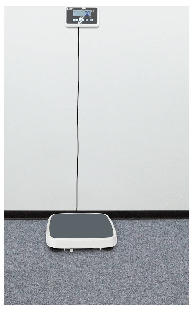 Elektronische Waage auf Teppichboden, mit digitaler Anzeige an der Wand.