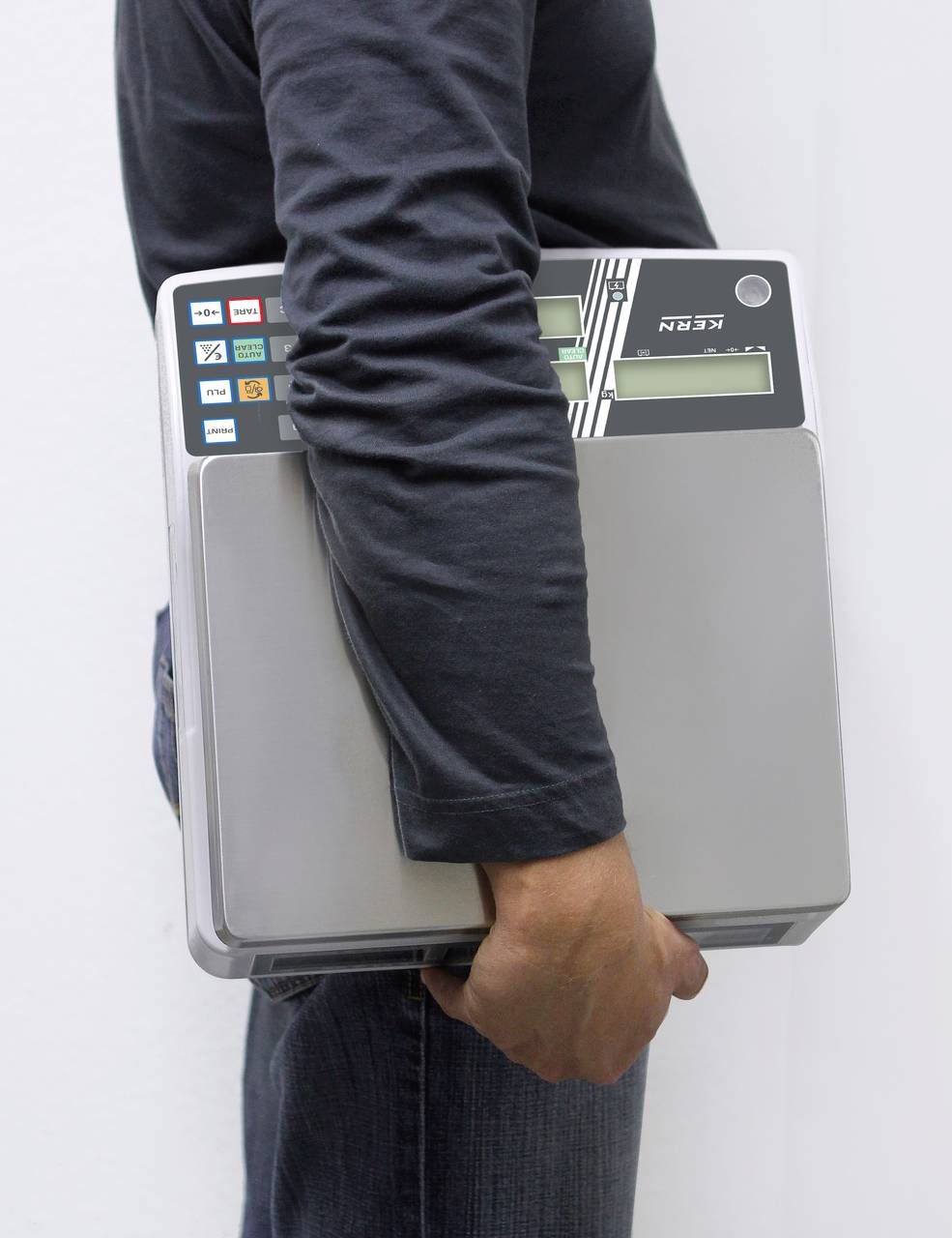 Eine Person trägt einen alten, tragbaren Computer mit Tastatur und Bildschirm. Der Computer hat Aufkleber und wirkt sperrig.