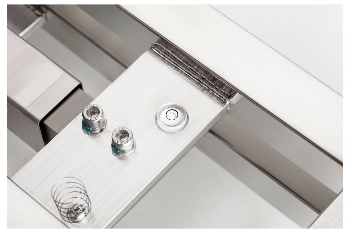 Metallische Oberflächenstruktur mit Schrauben und einer winzigen Feder. Technisches Detail eines Geräts oder einer Maschine.