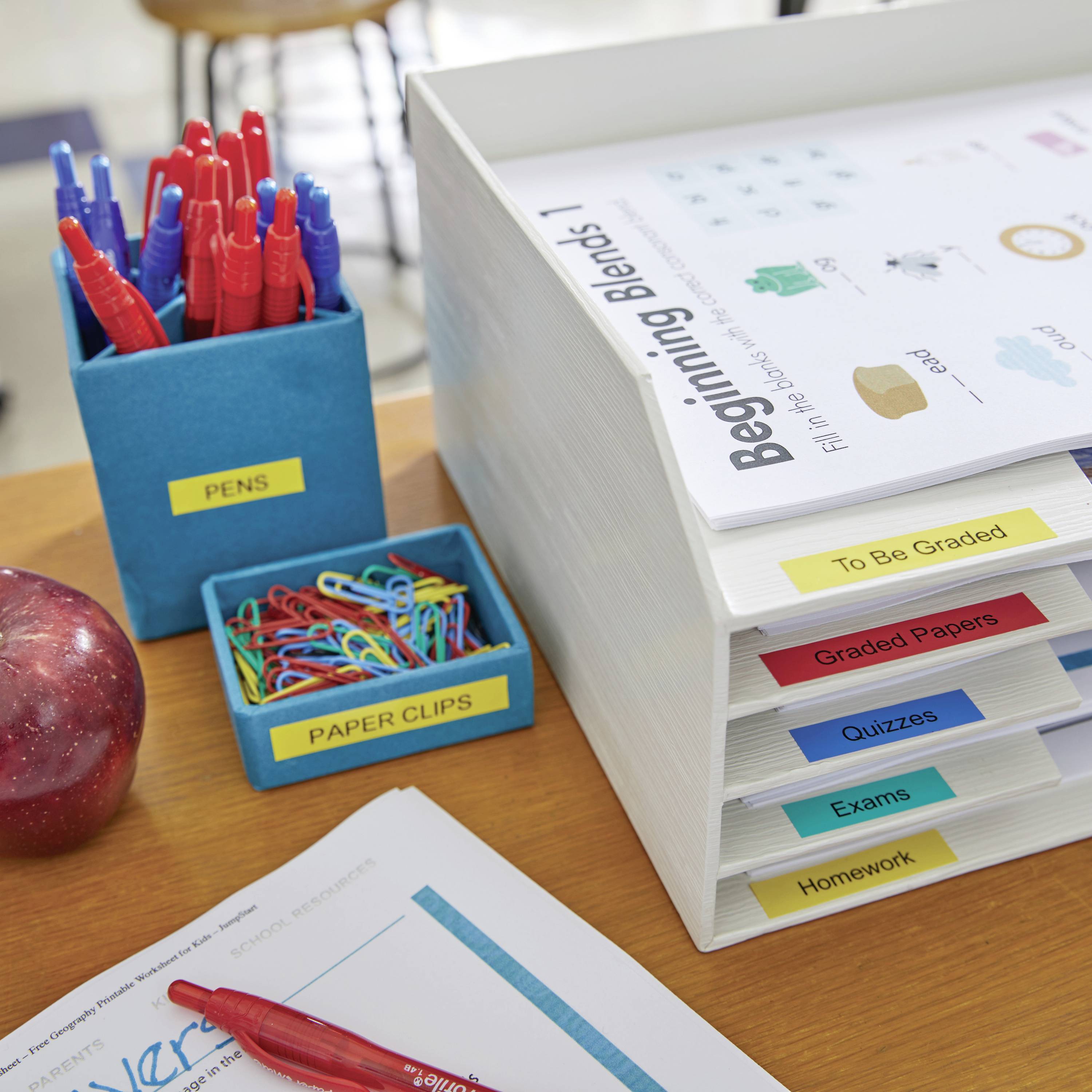 Ein Schreibtisch mit Stiften, Büroklammern und einer Ablage mit Fächern für verschiedene Arten von Dokumenten wie 'Hausaufgaben' und 'Prüfungen'.