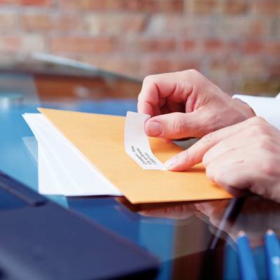 Person öffnet einen braunen Umschlag und zieht ein Blatt Papier mit dem Text 'Confidential' heraus. Im Hintergrund unscharfe Büroausstattung.