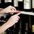 Person hängt ein rotes Etikett mit der Aufschrift 'Cabernet' an ein Weinregal. Verschiedene Weinflaschen sind sichtbar.