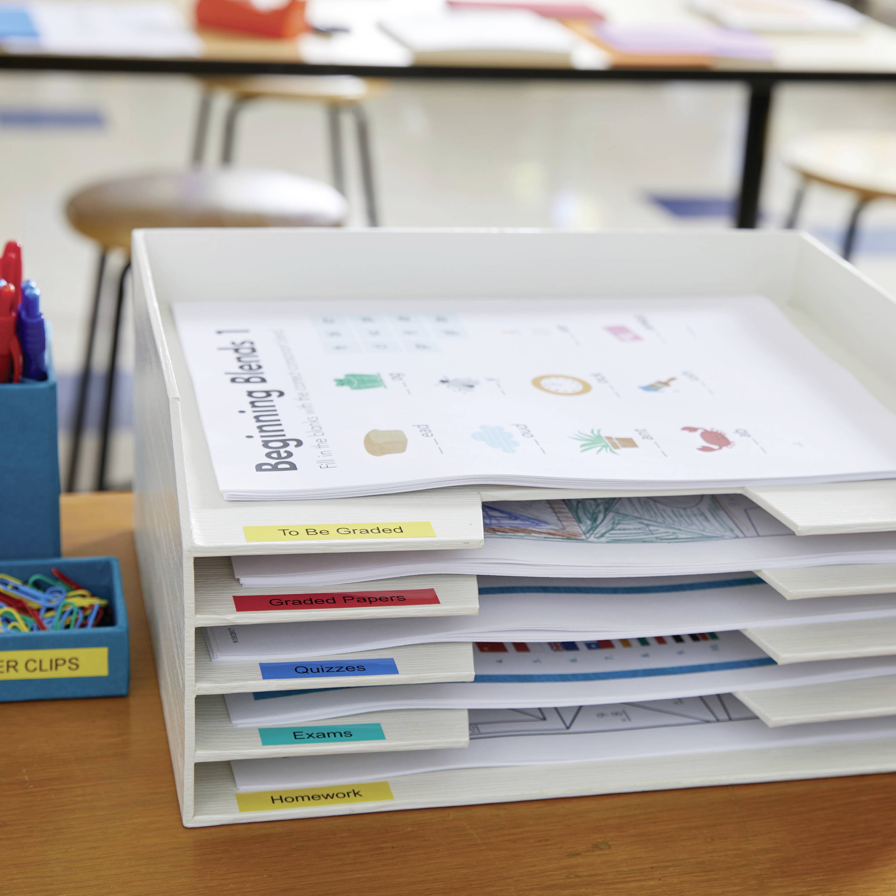 In einem weißen Dokumentenablagesystem sind Fächer mit den Beschriftungen 'To Be Graded', 'Graded Papers', 'Exams', 'Homework' zu sehen.