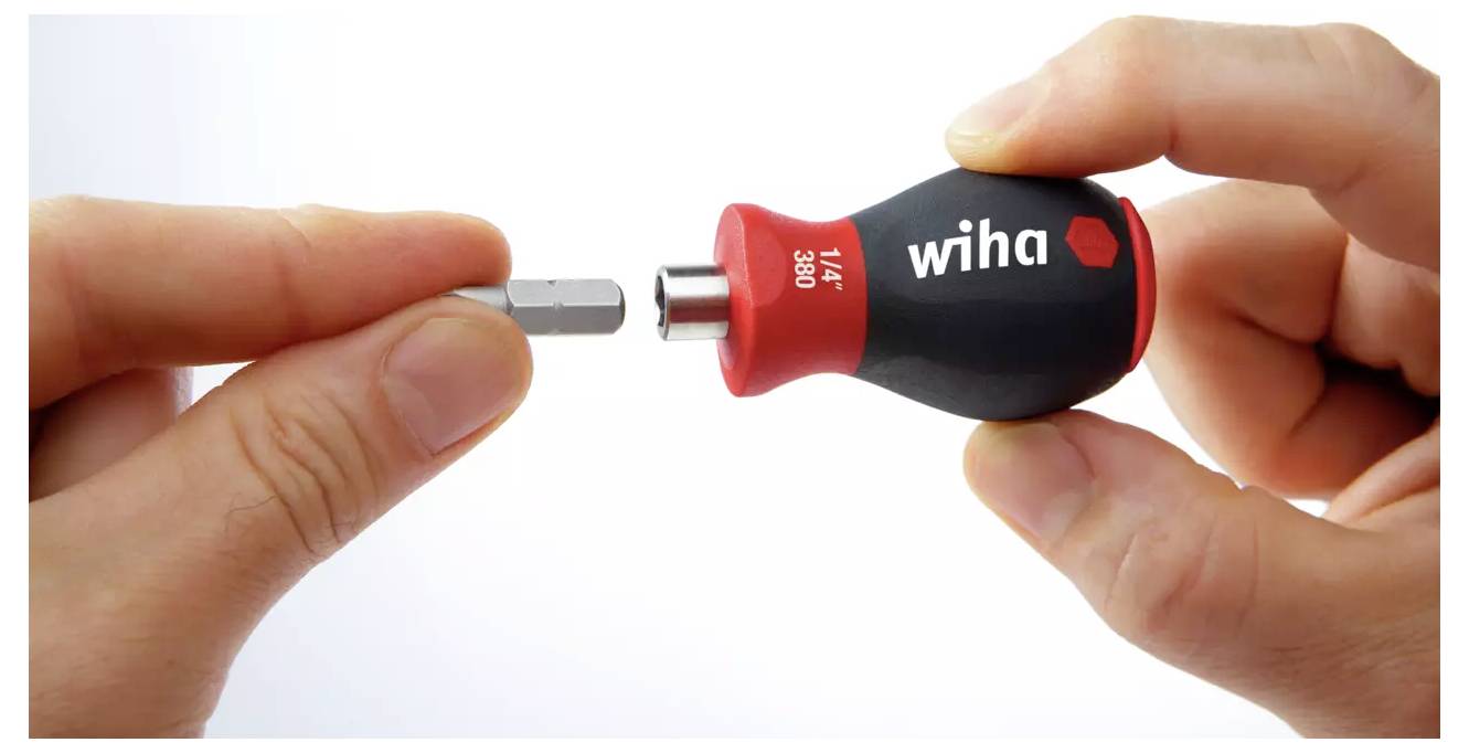 Eine Person hält einen kleinen Wiha-Schraubendrehergriff und ein separates Bit in der Hand, um die Befestigung zu demonstrieren und das kompakte Design des Werkzeugs hervorzuheben.
