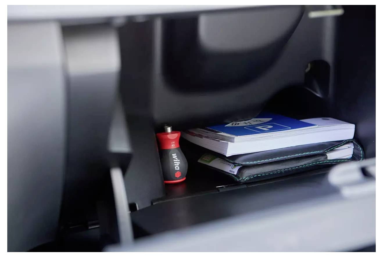 Handschuhfach eines Autos mit einem rot-schwarzen Multitool, einem blauen Notizblock und einer Reißverschlusstasche im Inneren.