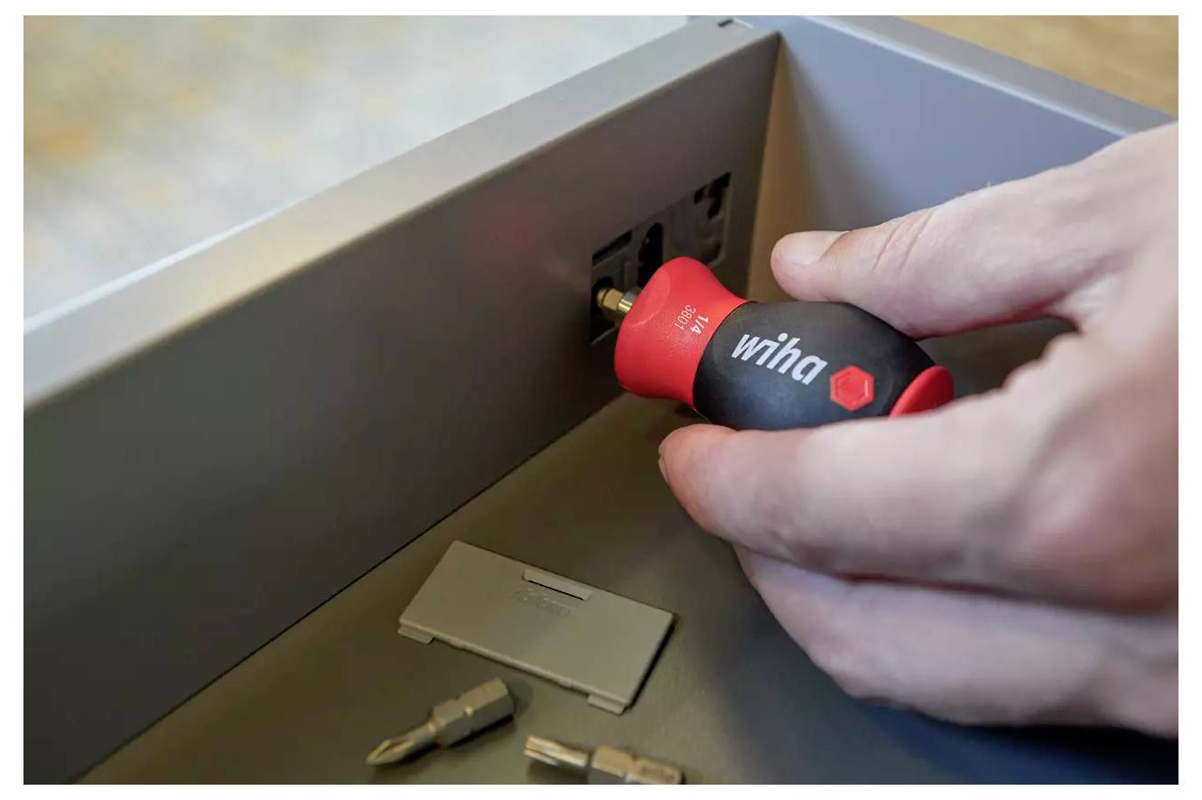 Eine Person verwendet einen Schraubendreher, um eine Schraube in einem Metallpanel festzuziehen. Ein paar Schraubendreherbits liegen in der Nähe auf der Oberfläche.