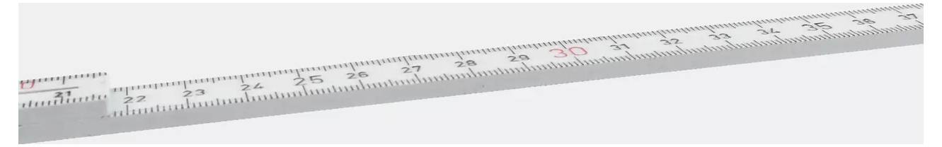 Ein silbernes Stahllineal mit Zentimetermarkierungen, diagonal über einem hellen Hintergrund angeordnet.