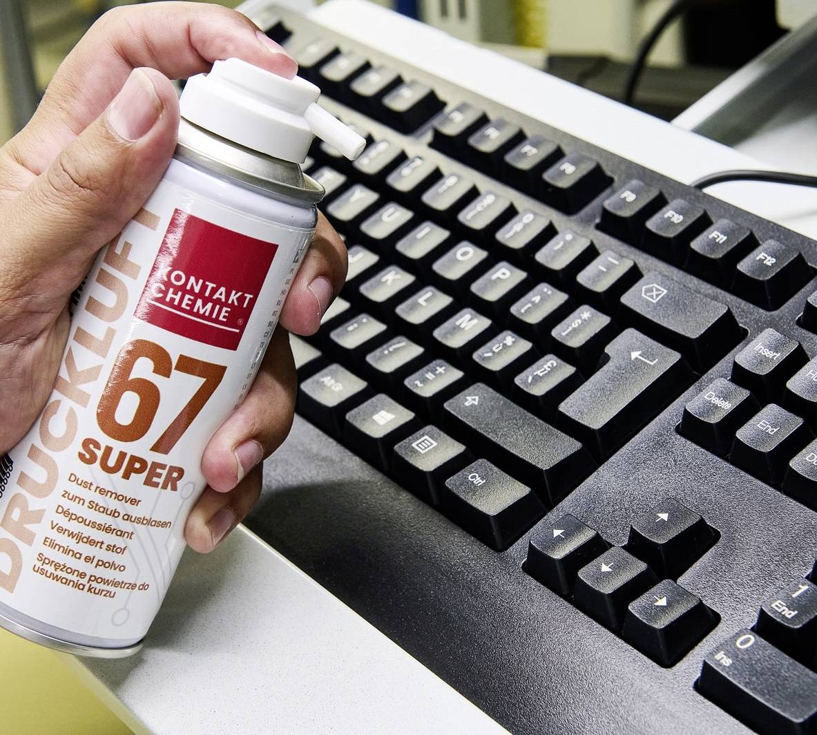 Eine Person hält eine Dose Druckluftspray und reinigt eine Computertastatur.