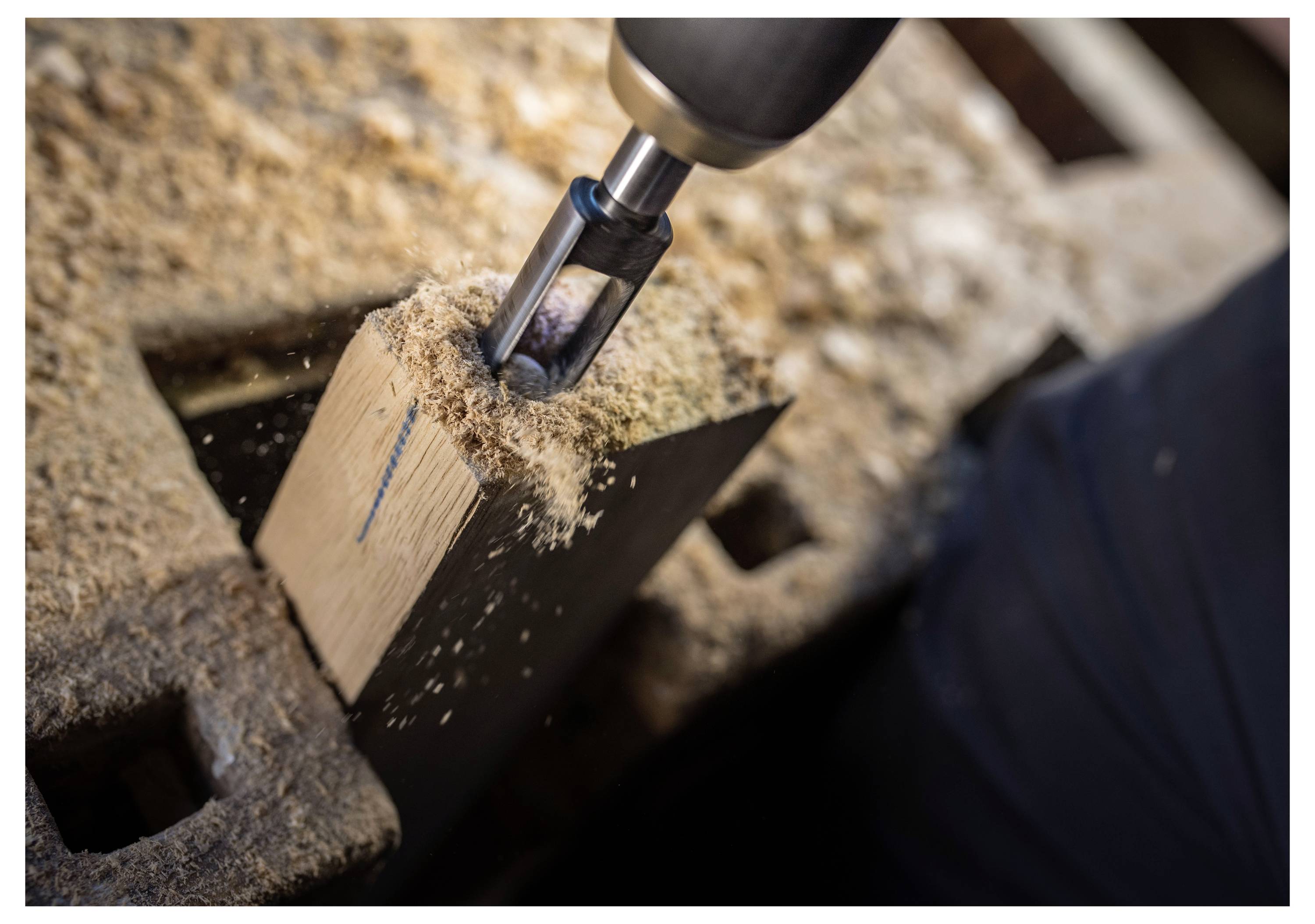 Nahaufnahme eines Elektroschraubers-Bohrers, der in einen Holzbalken eindringt, wobei Holzspäne wegfliegen.