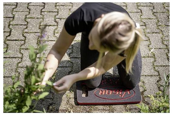 Eine Person kniet auf einer 'VIKOS' Matte und kümmert sich um Pflanzen auf einer gepflasterten Außenfläche.