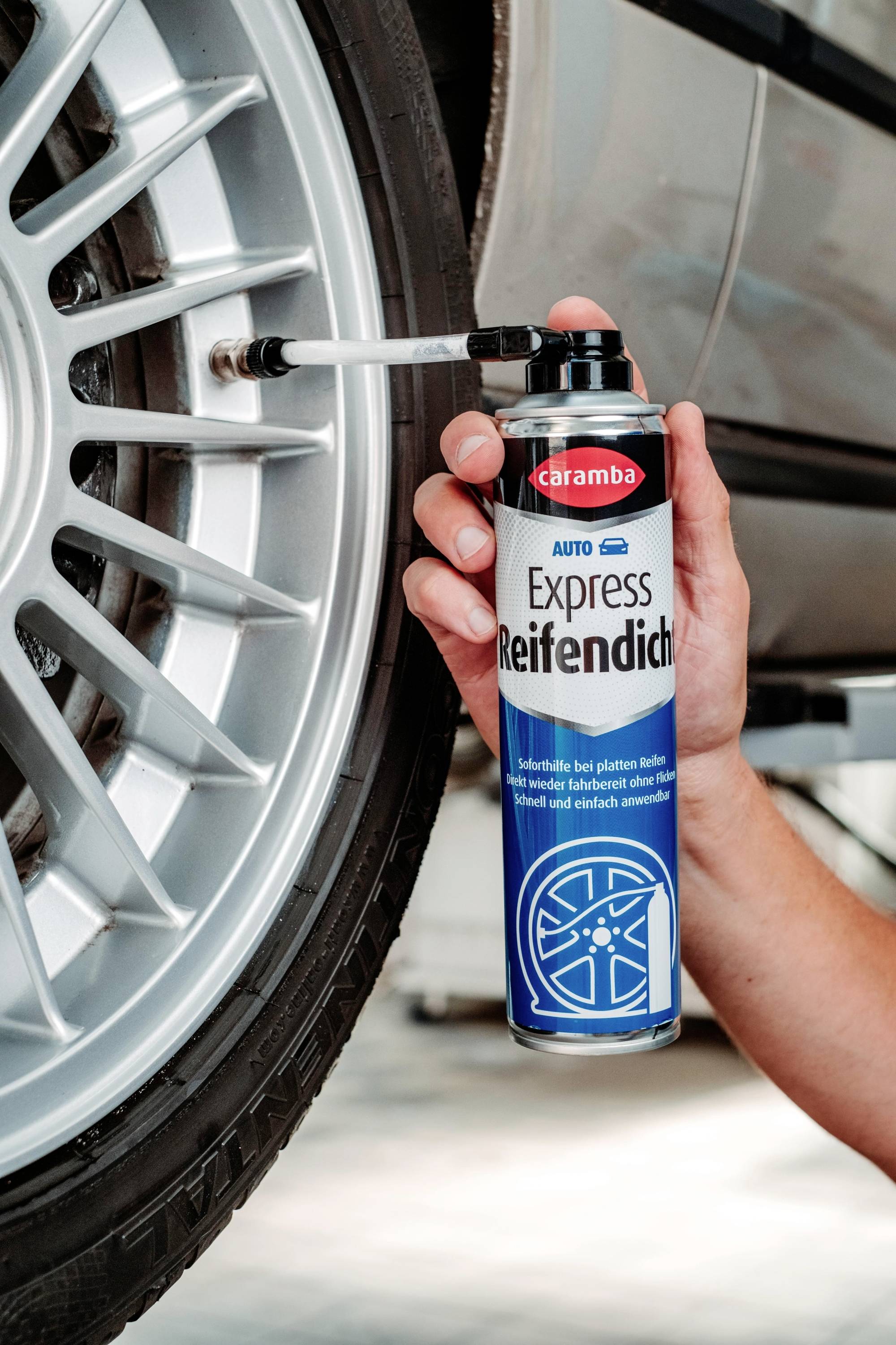 Eine Person hält eine Dose mit der Aufschrift "Express Reifendicht" in der Nähe eines Autoreifen und verwendet sie, um eine Dichtungsmasse auf die Felge aufzutragen.