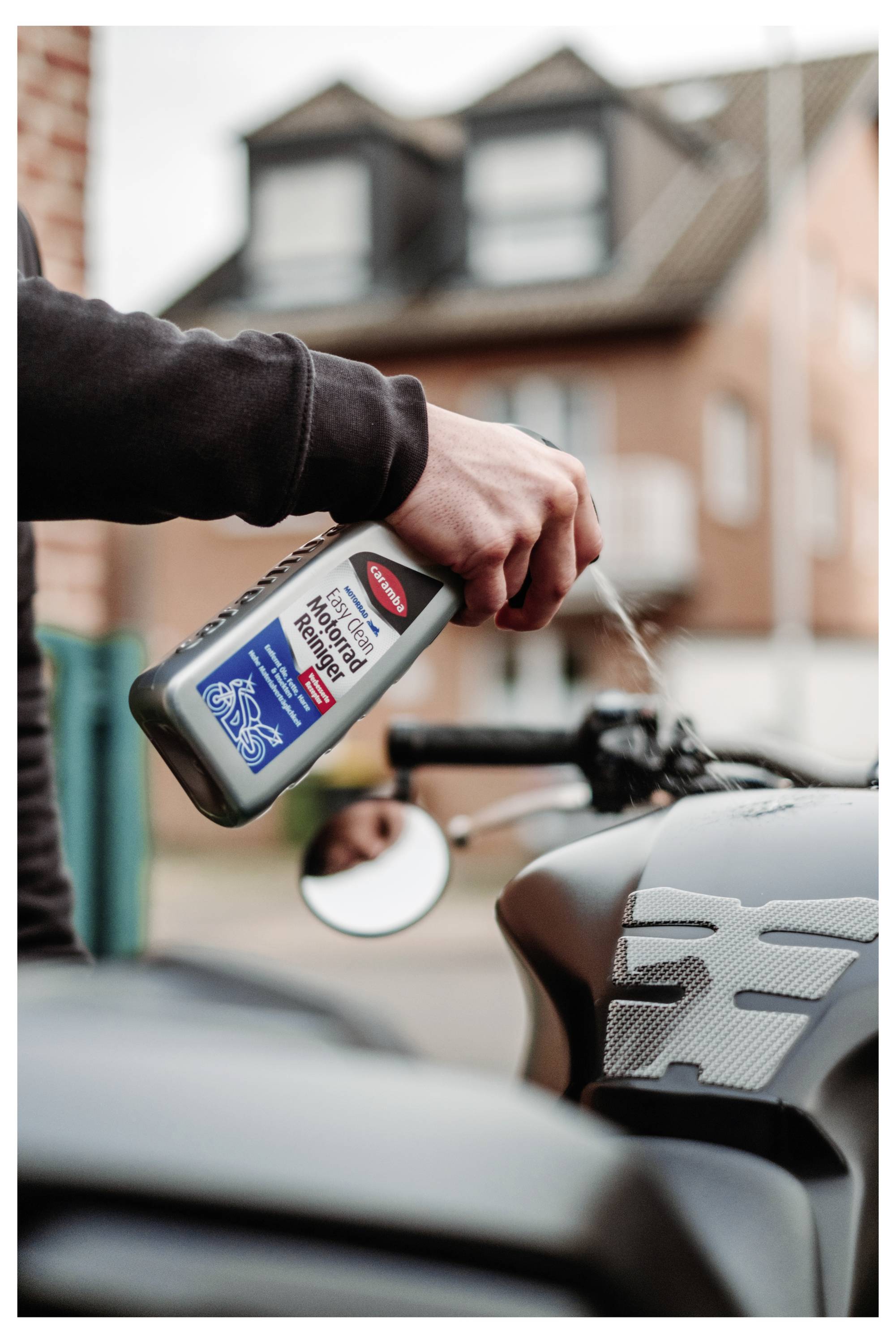 Eine Hand gießt Motoröl aus einer Flasche in ein Motorrad auf einer Wohnstraße.