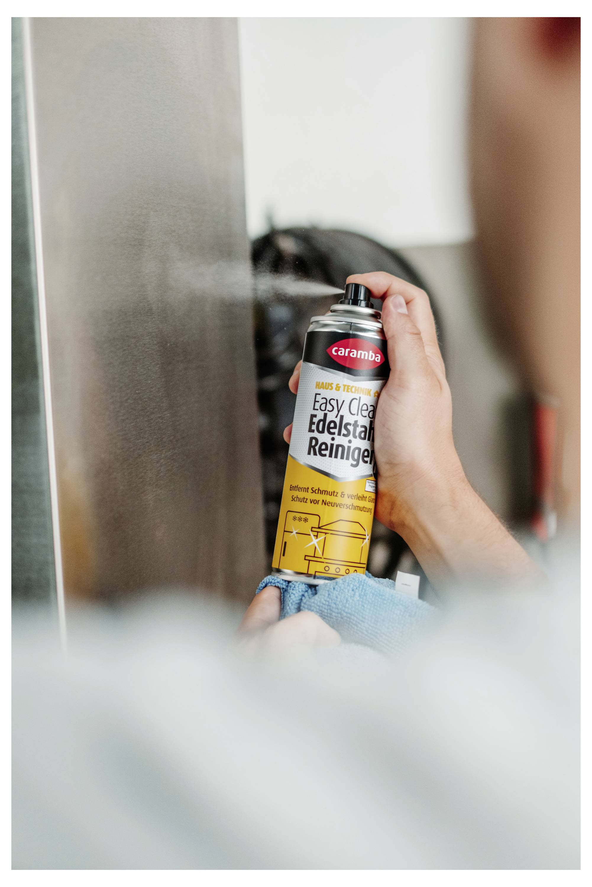 Person sprüht 'Easy Clean Edelstahl Reiniger' Reiniger auf eine Edelstahloberfläche, während sie diese mit einem Tuch abwischt.