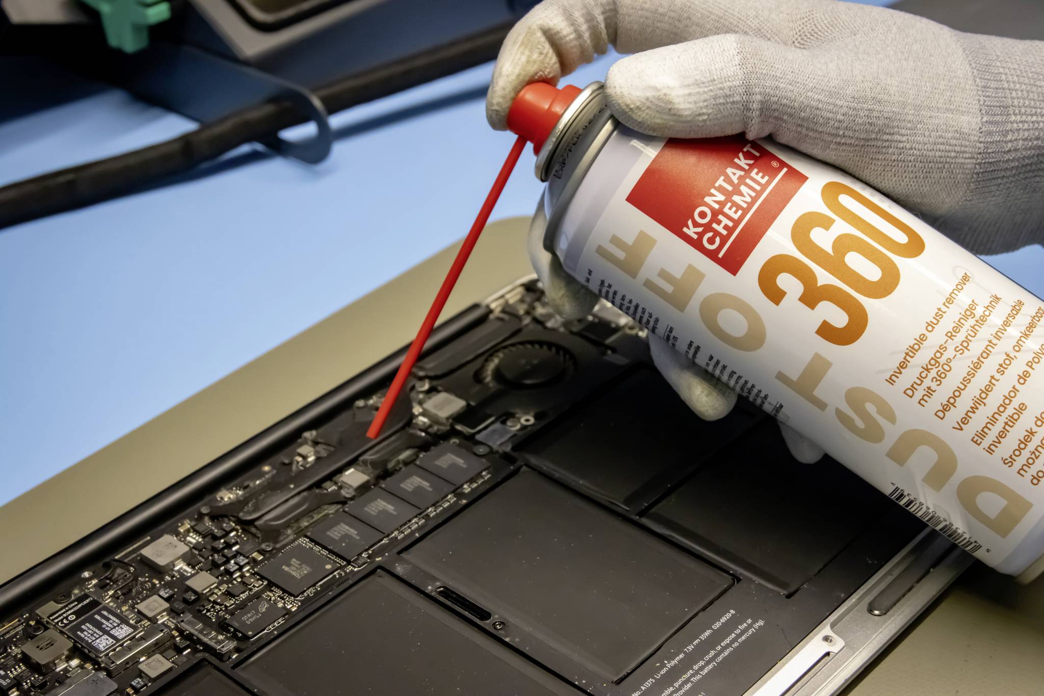 Eine Person trägt Handschuhe und verwendet Druckluftspray, um die Innenseite eines Laptops zu reinigen.