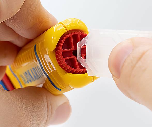 Zwei Hände montieren eine gelbe Sicherheitsvorrichtung aus Kunststoff mit einem roten Rad und einer transparenten Abdeckung, Nahaufnahme, die Präzision zeigt.