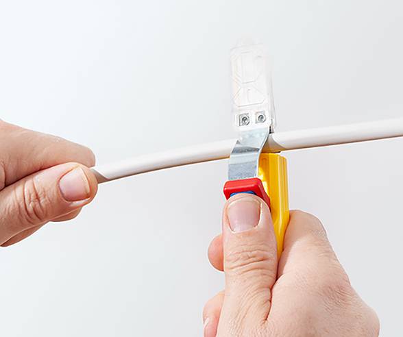 Hände, die eine Abisolierzange benutzen, um die Isolierung von einem weißen Elektrokabel zu entfernen, wobei Präzision und Sicherheit bei elektrischen Arbeiten hervorgehoben werden.